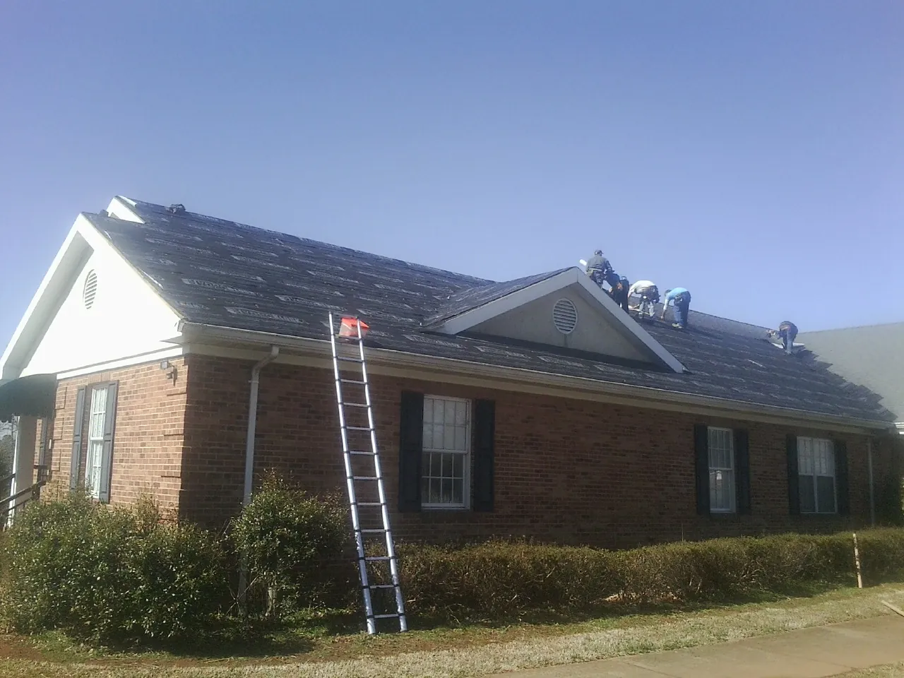 Crew tearing shingles off a brick ranch roof with a ladder set — Emergency Roof Repair work by our crew in Fuquay Varina