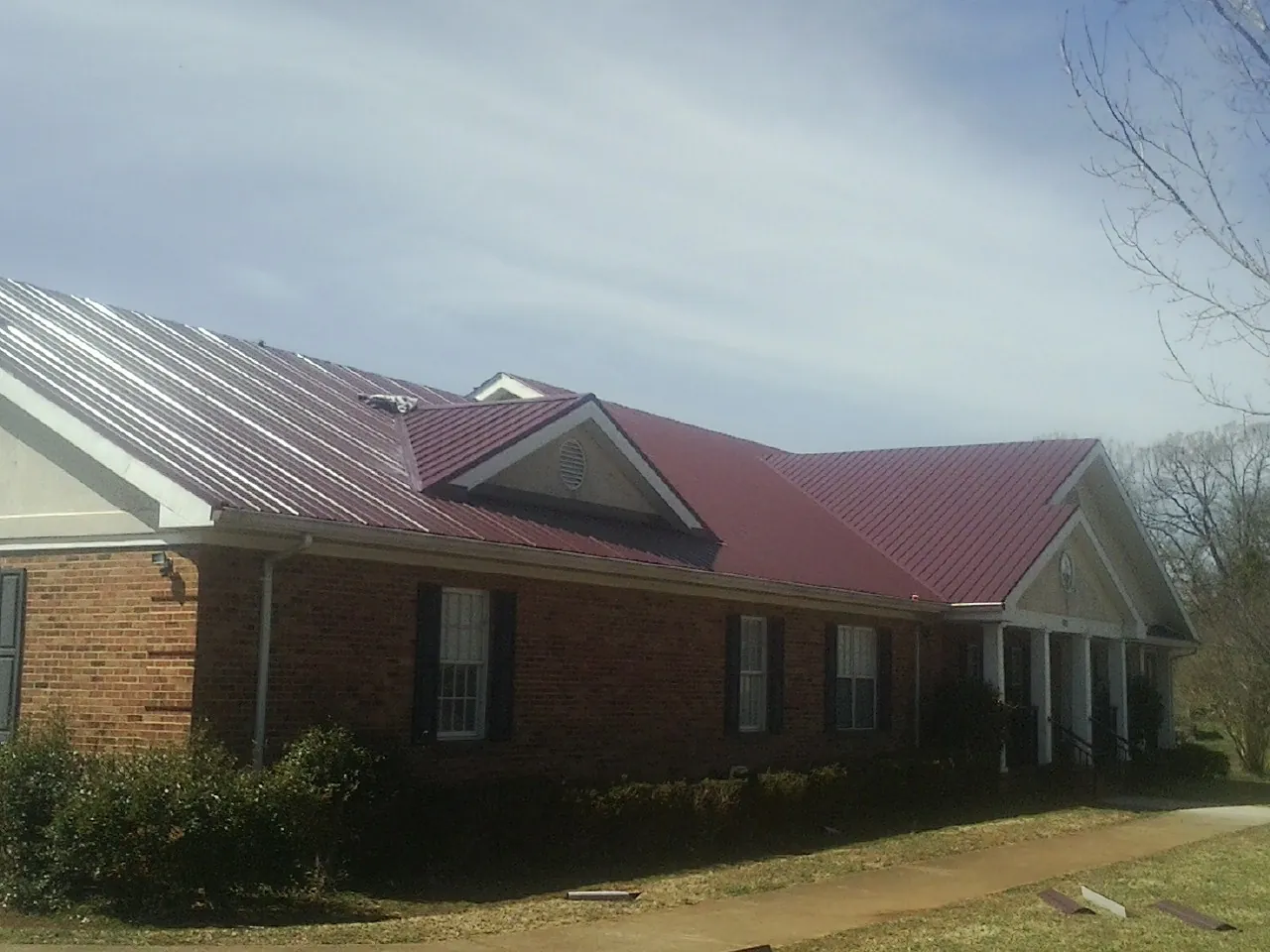 Red metal roof with gabled entries on a long brick building, from a Hail Damage Roof Repair job in Fuquay Varina