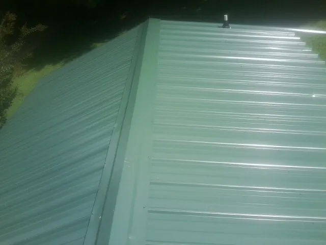New green metal panels meeting at the ridge of a roof — Flat Roof Repair work by our crew in Fuquay Varina