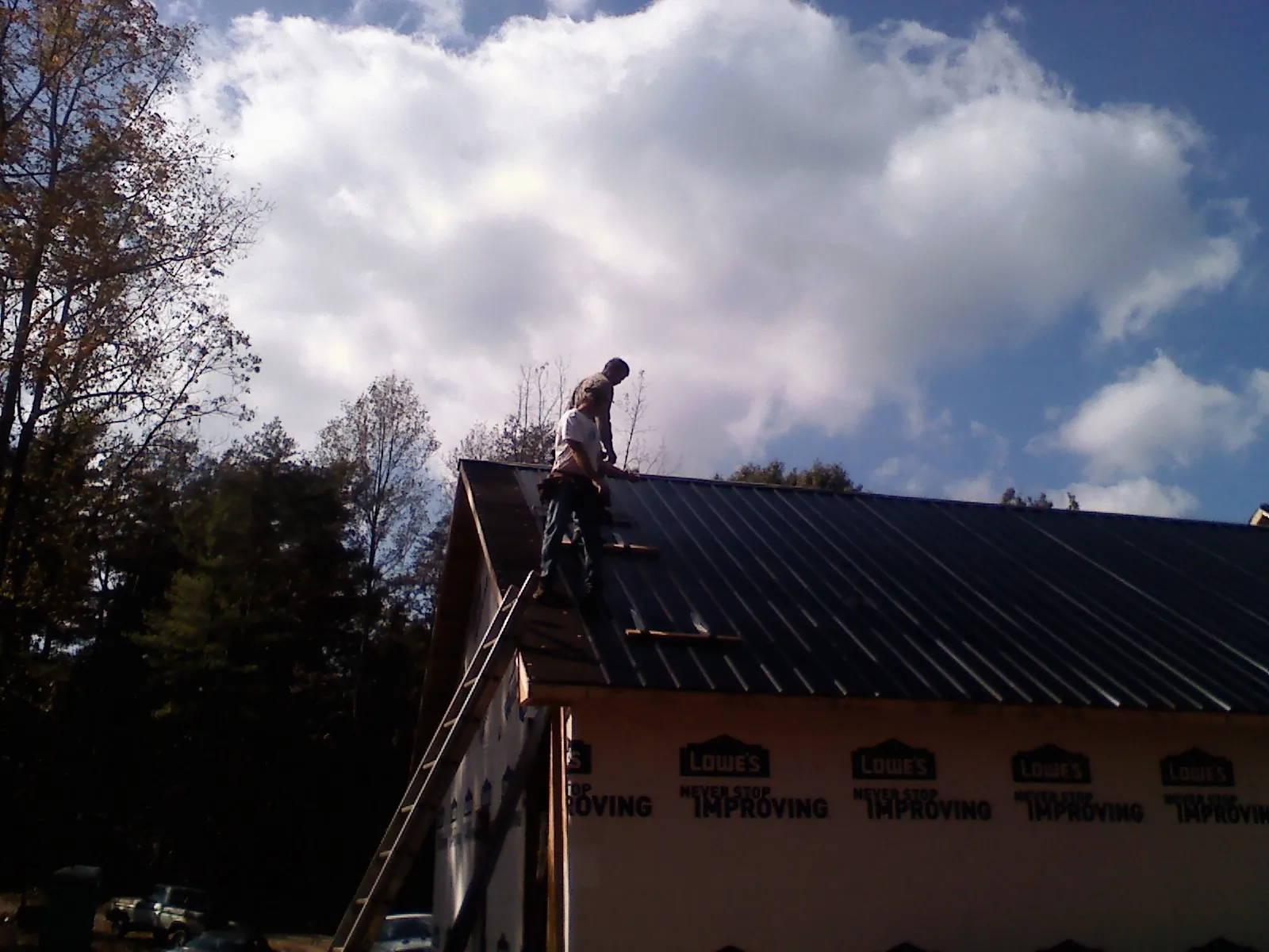 Roofer fastening dark metal panels high against a cloudy sky, from a Roof Inspection job in Fuquay Varina