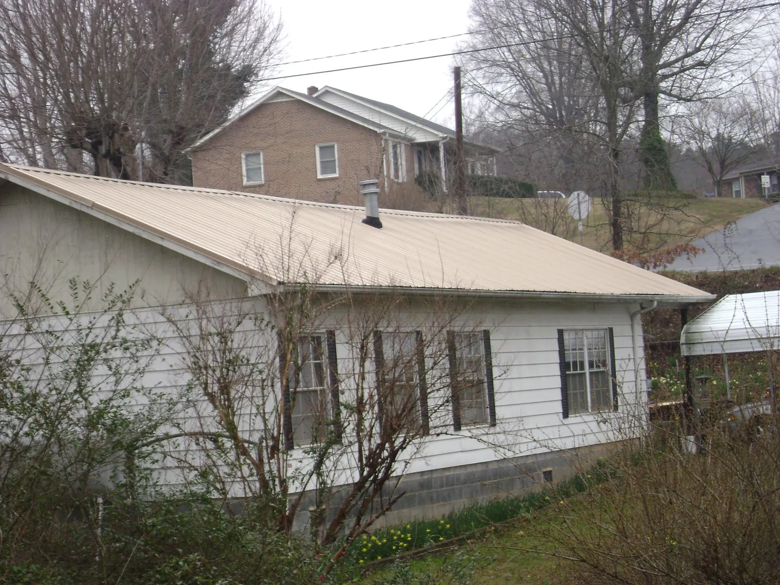 Tan metal roof on a white sided house set into a hillside — Commercial Roofing by Roofing Brothers in Fuquay Varina